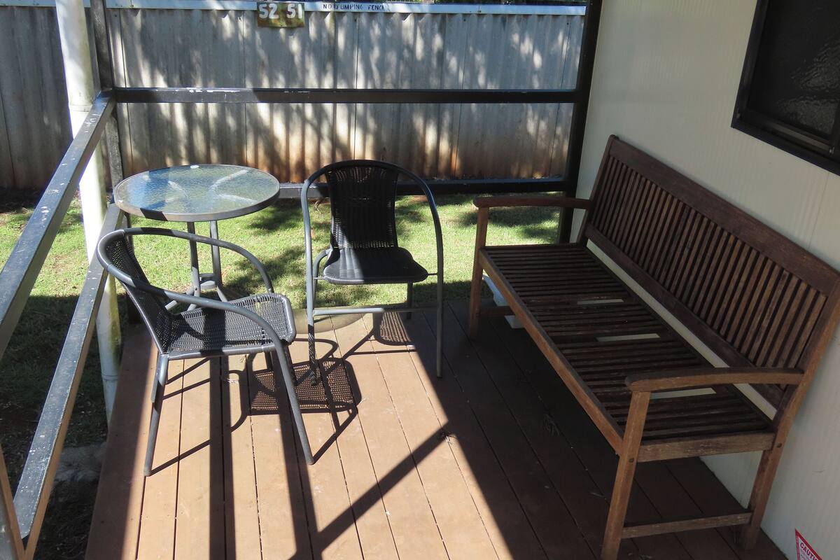 Une terrasse en bois avec une table ronde et deux chaises, un banc en bois et, au fond, une clôture en bois.