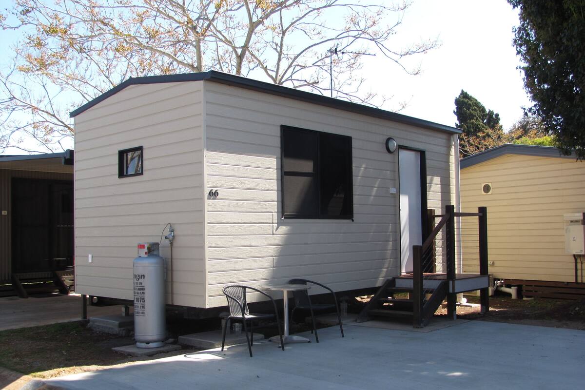 Une petite maison mobile d’un seul étage, dotée d’un porche à l’avant, d’un chauffe-eau et d’une chaise.