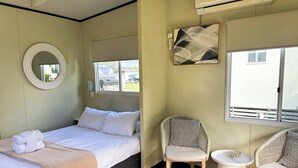 A hotel room with a bed, a round mirror, a chair, a small table, and a window with a view of buildings. - BIG4 Toowoomba Holiday Park (Harristown)