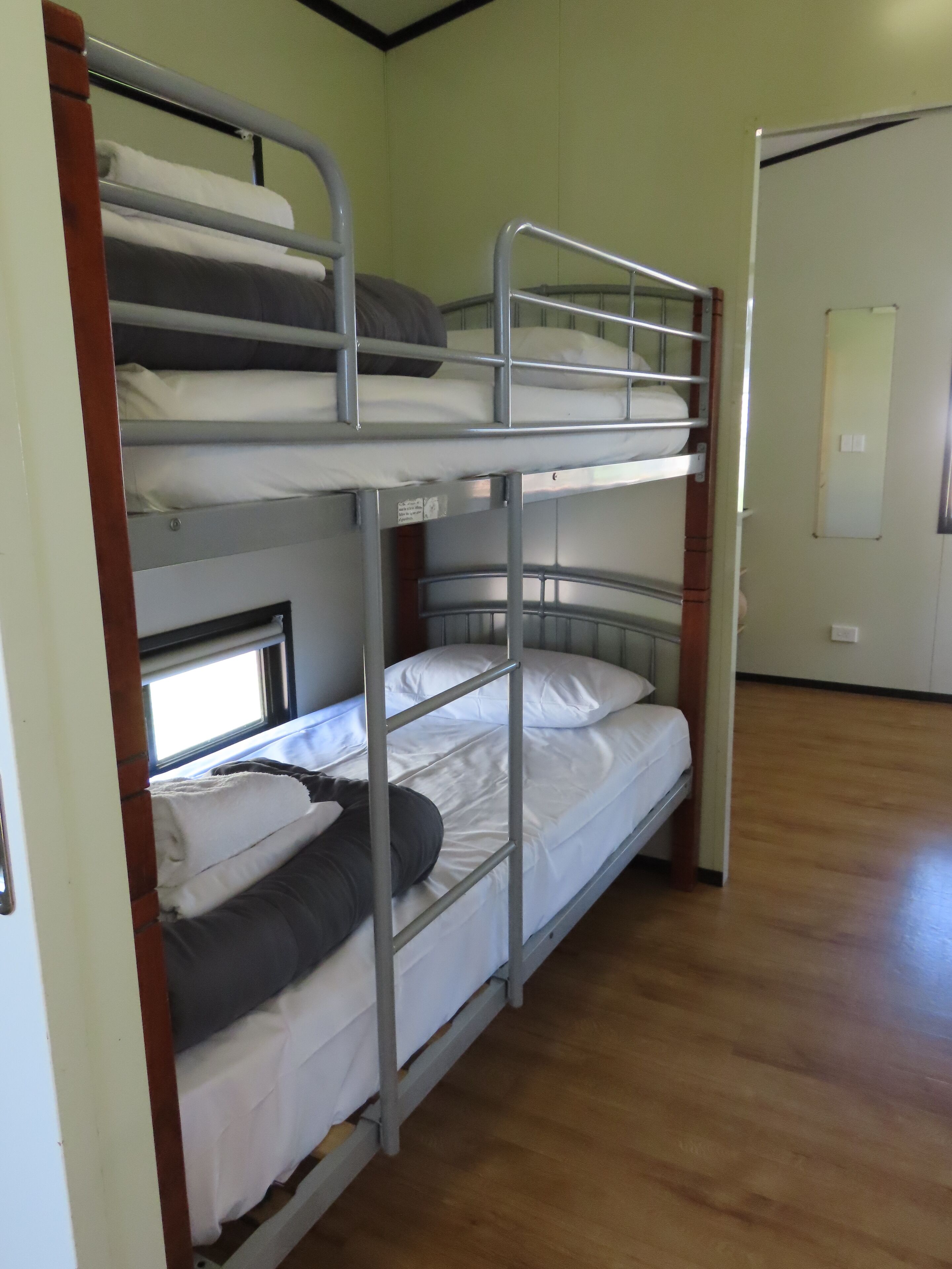 Habitación con literas de dos niveles, suelo de madera y una puerta al fondo.
