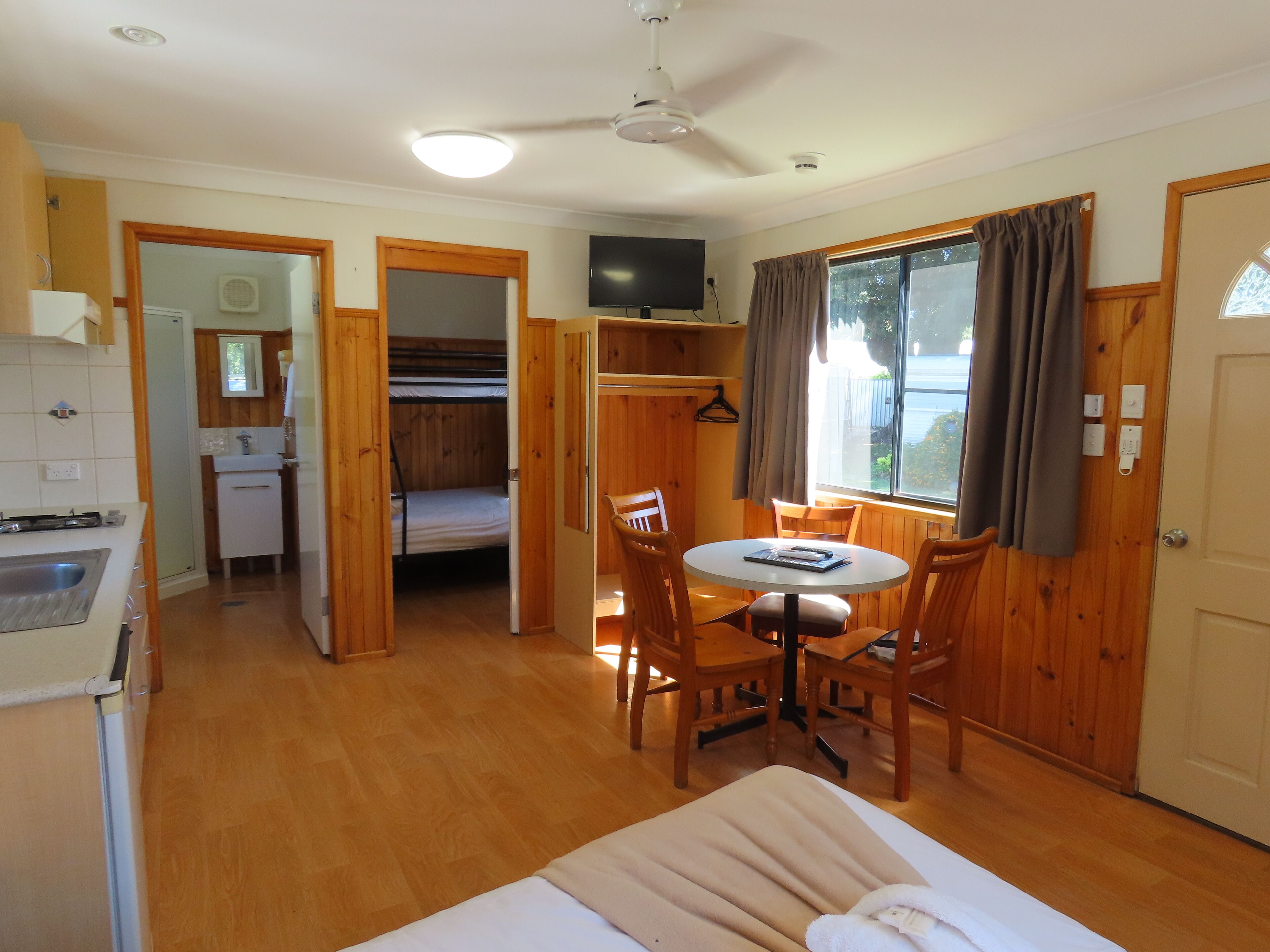 A compact room with a bunk bed, a small kitchenette, a dining area with a table and chairs, and a window with curtains.