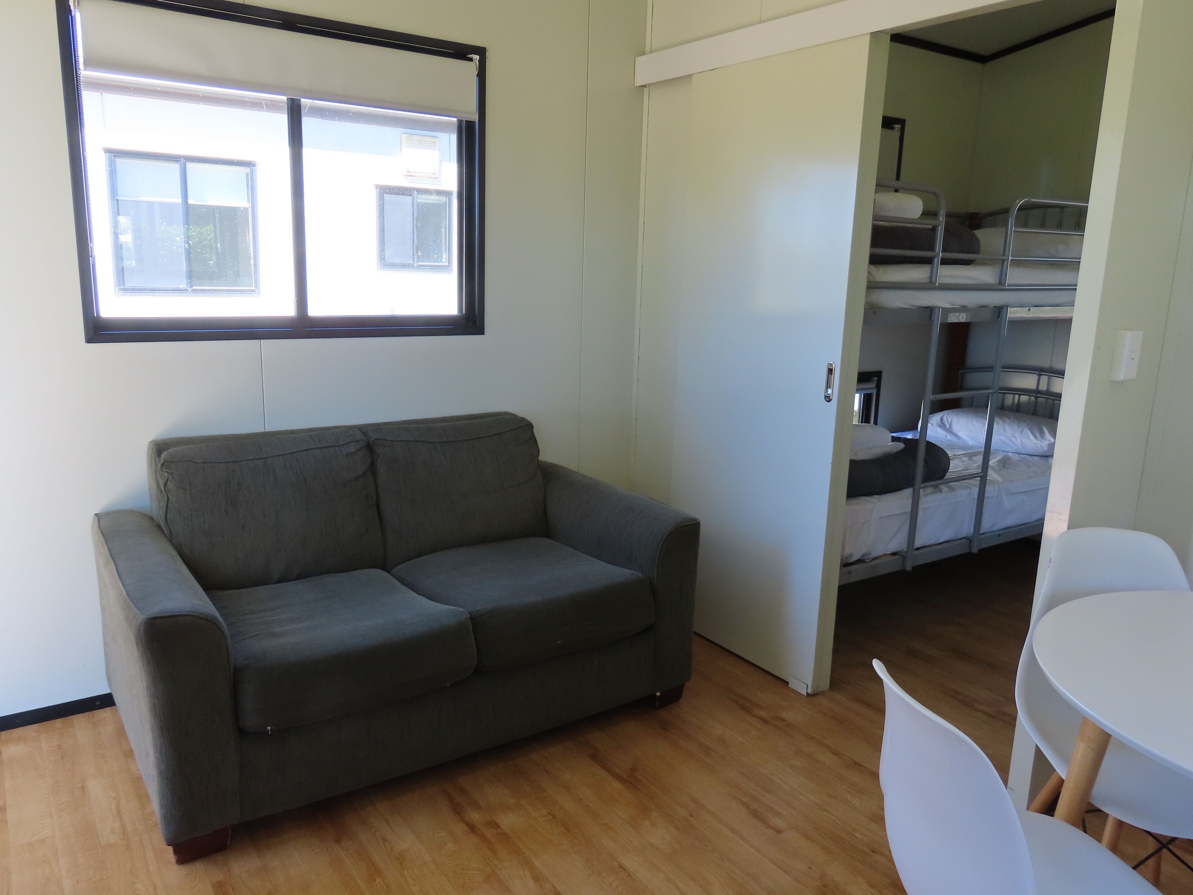 Una habitación con un sofá gris, una mesa blanca y una litera con dos camas.