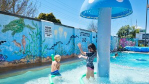 A water play area with a mural of sea creatures on the wall, a sign prohibiting headwear under water, and a pool with people playing. - BIG4 Toowoomba Holiday Park (Harristown)