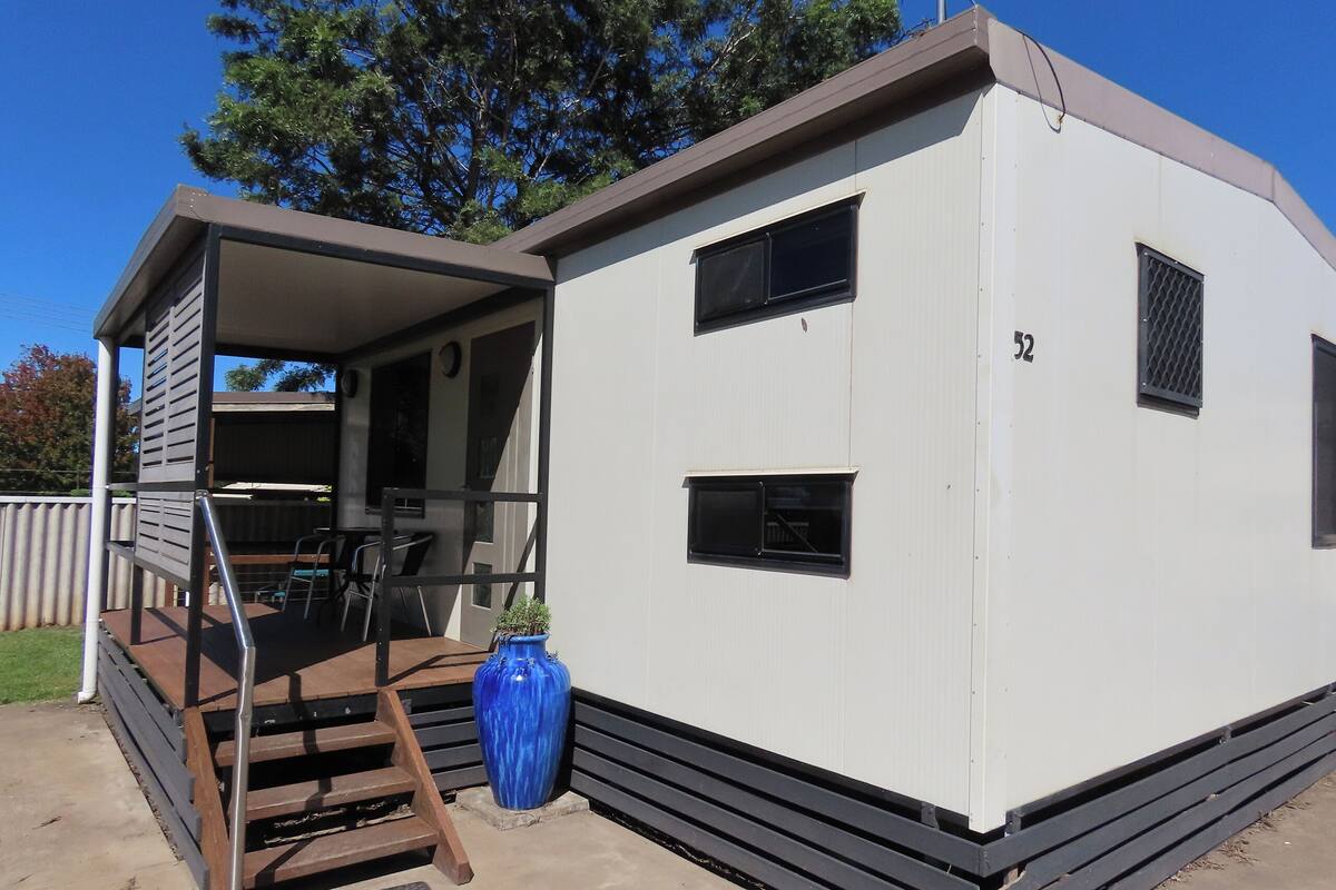 Une maison mobile avec une véranda, un vase bleu et le numéro 52 peint sur le côté.