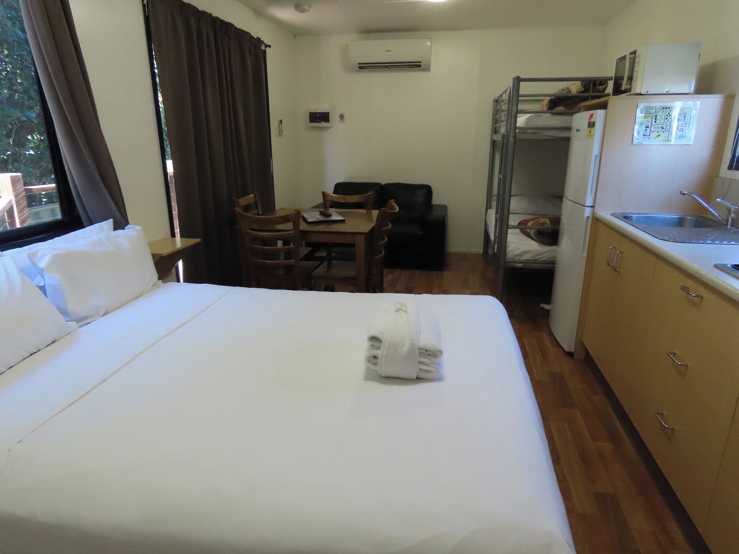 A hotel room with a bed, a desk, a chair, a bunk bed, and a kitchenette.