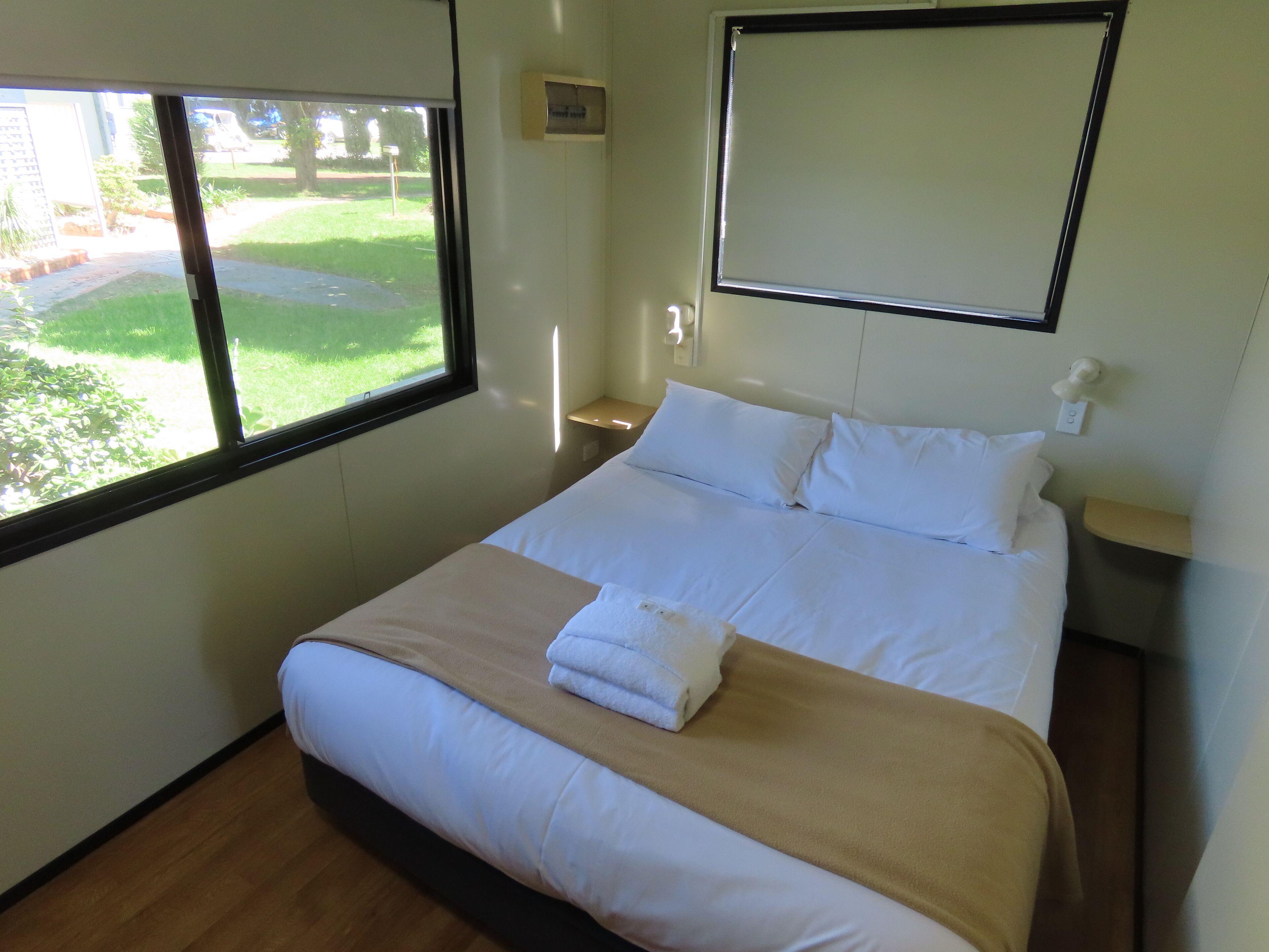 A hotel room with a bed, a window, a bedside table, and a nightstand.