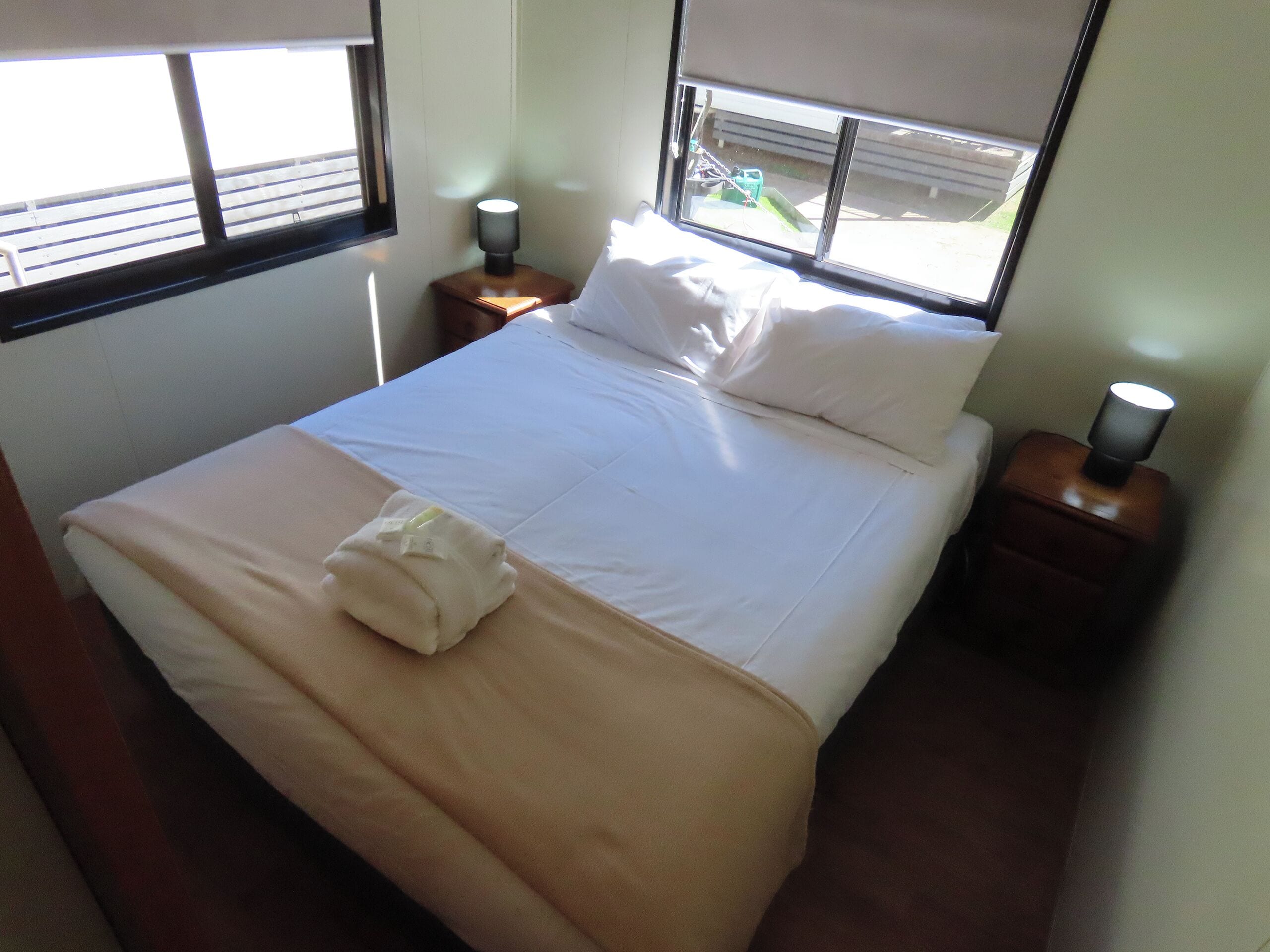 A neatly made bed with white linens, a folded towel, and two bedside lamps on wooden nightstands.