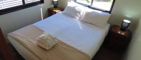 A neatly made bed with white linens, a folded towel, and two bedside lamps on wooden nightstands.