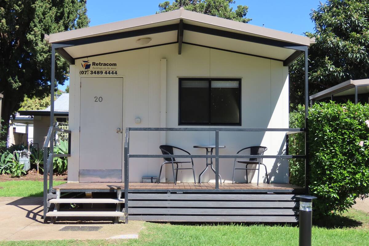 Un petit bâtiment d’un seul étage, doté d’un toit plat, d’une porte portant le numéro 20 et d’une enseigne indiquant qu’il s’agit d’un bâtiment Retracom. On peut voir deux chaises et une table à l’extérieur du bâtiment.