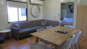 A room with a wooden table, white chairs, a grey sofa, and a ceiling fan. - BIG4 Toowoomba Holiday Park (Harristown)