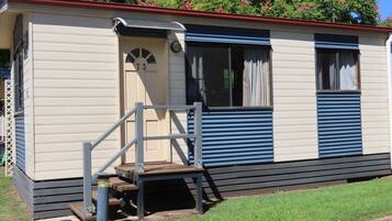 A mobile home with a number '73' on the door, a small porch with a bench, and a window with curtains.