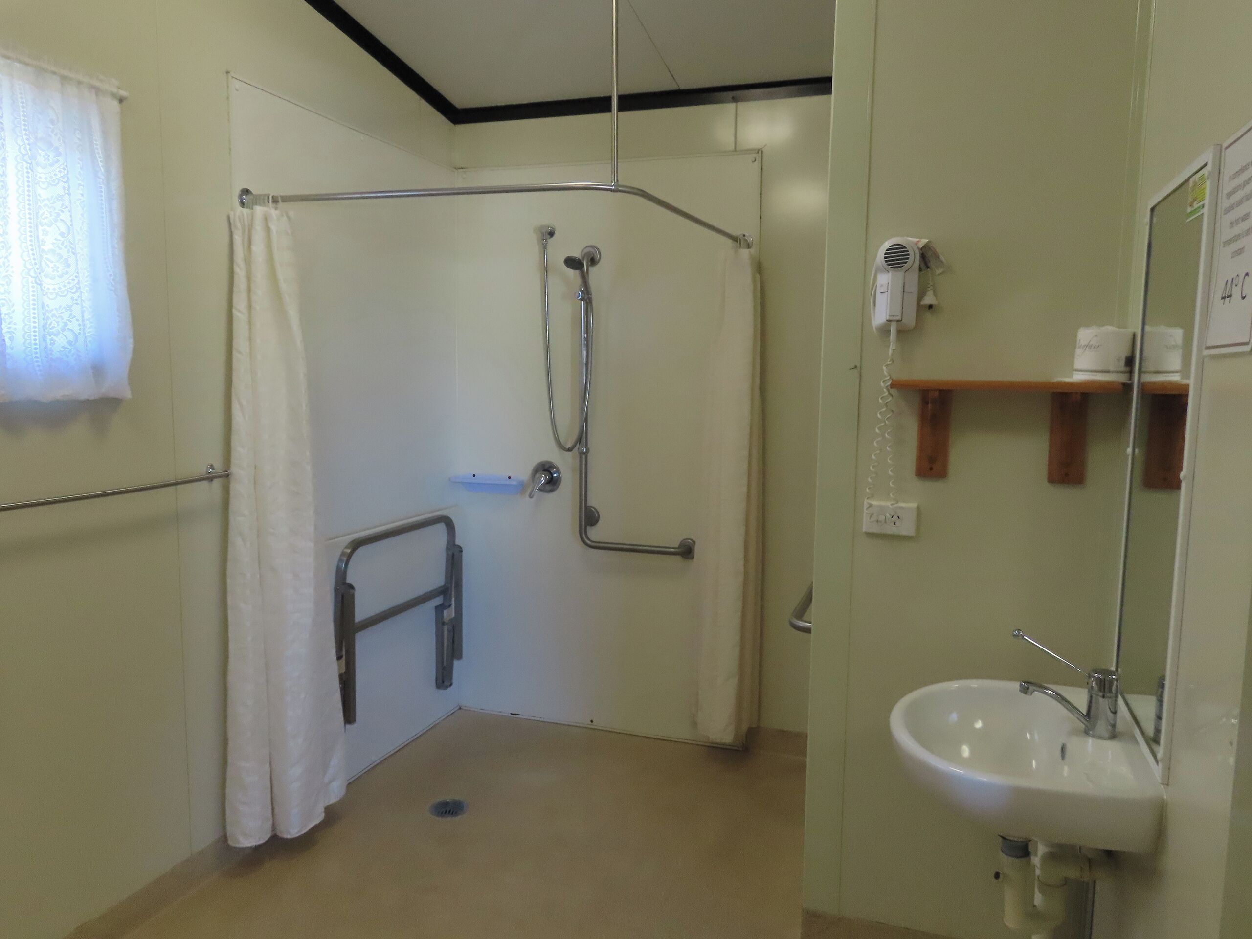 A bathroom with a shower, a sink, and a hairdryer on a shelf.