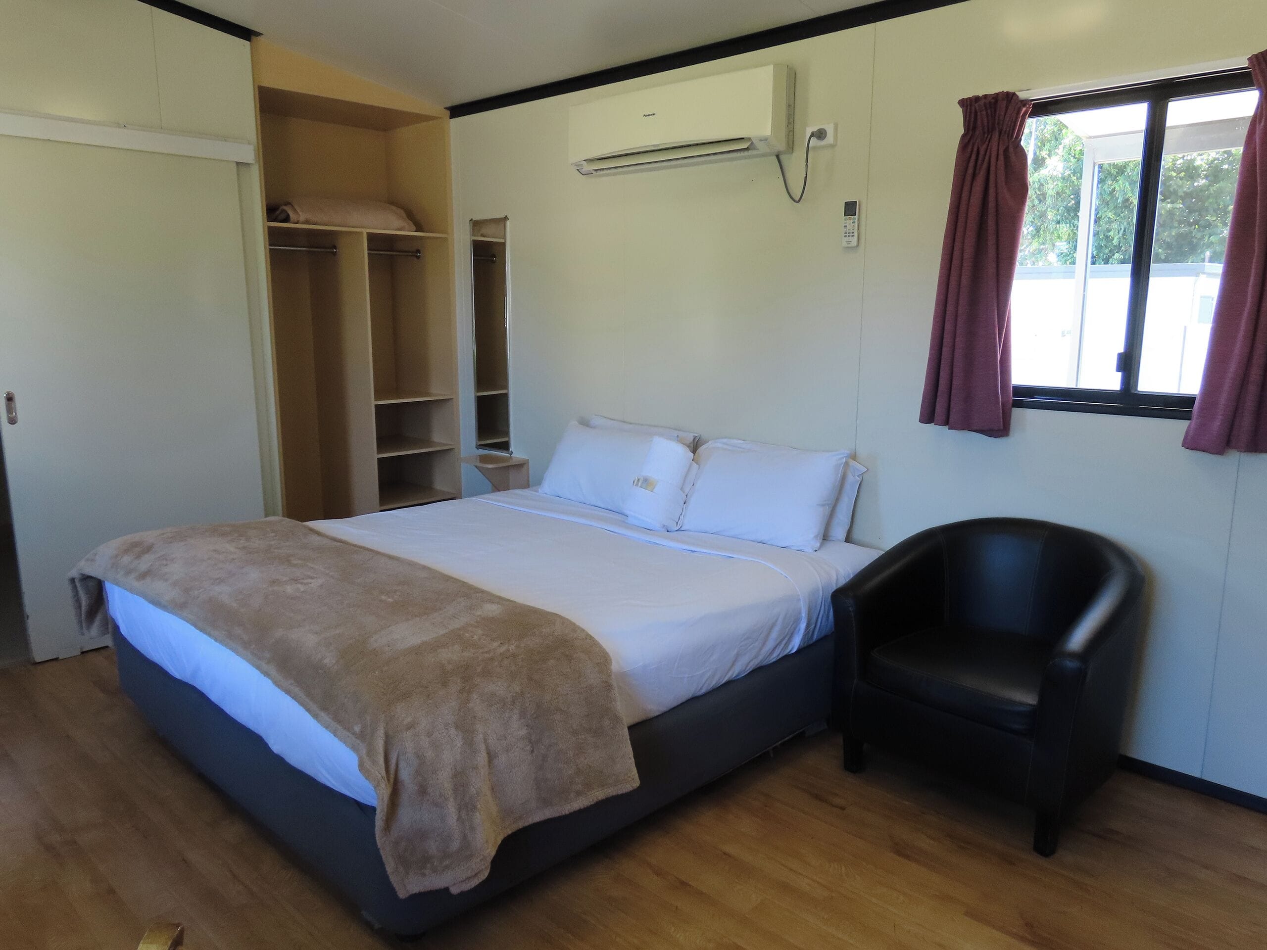Un dormitorio con cama, una silla, un armario y un equipo de aire acondicionado.