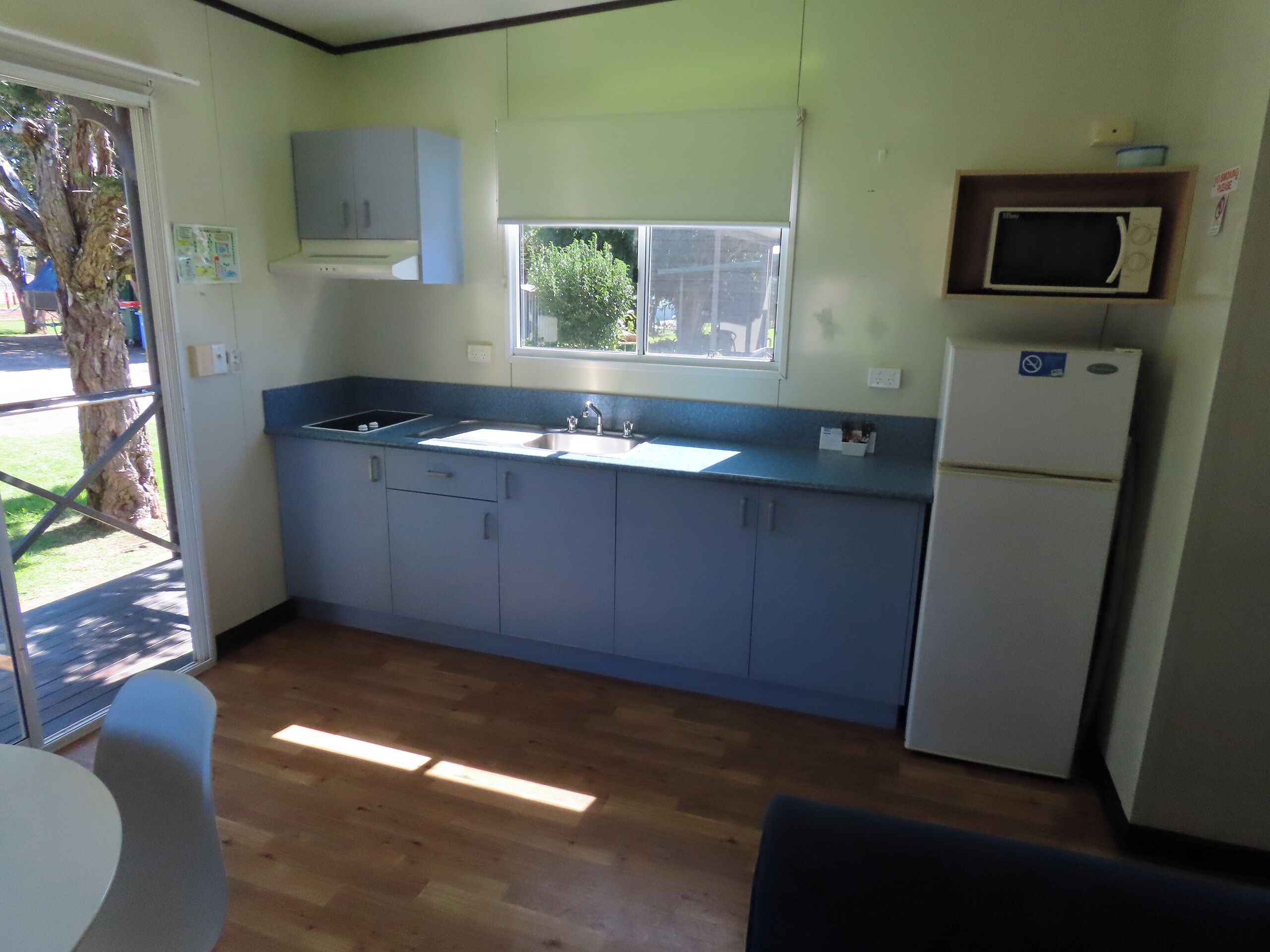 A kitchen with a sink, cabinets, a window, and a microwave.