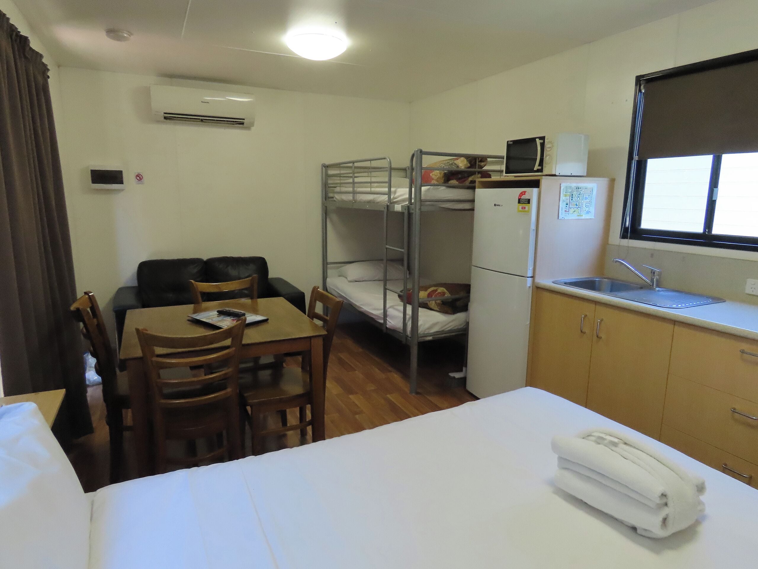 Ein kleines Hotelzimmer mit Etagenbetten, einer kleinen Küchenzeile, einem Esstisch mit Stühlen und einem Einzelbett.