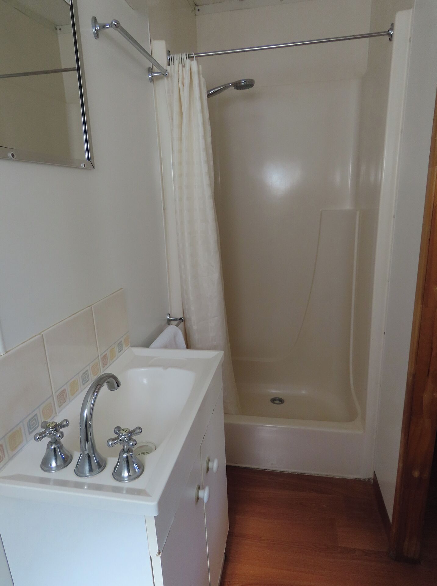 Une salle de bain avec un lavabo blanc, deux robinets, un miroir et un espace douche séparé par un rideau.