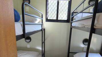 A narrow room with bunk beds, a small window with a grid pattern, and a door with a round handle.