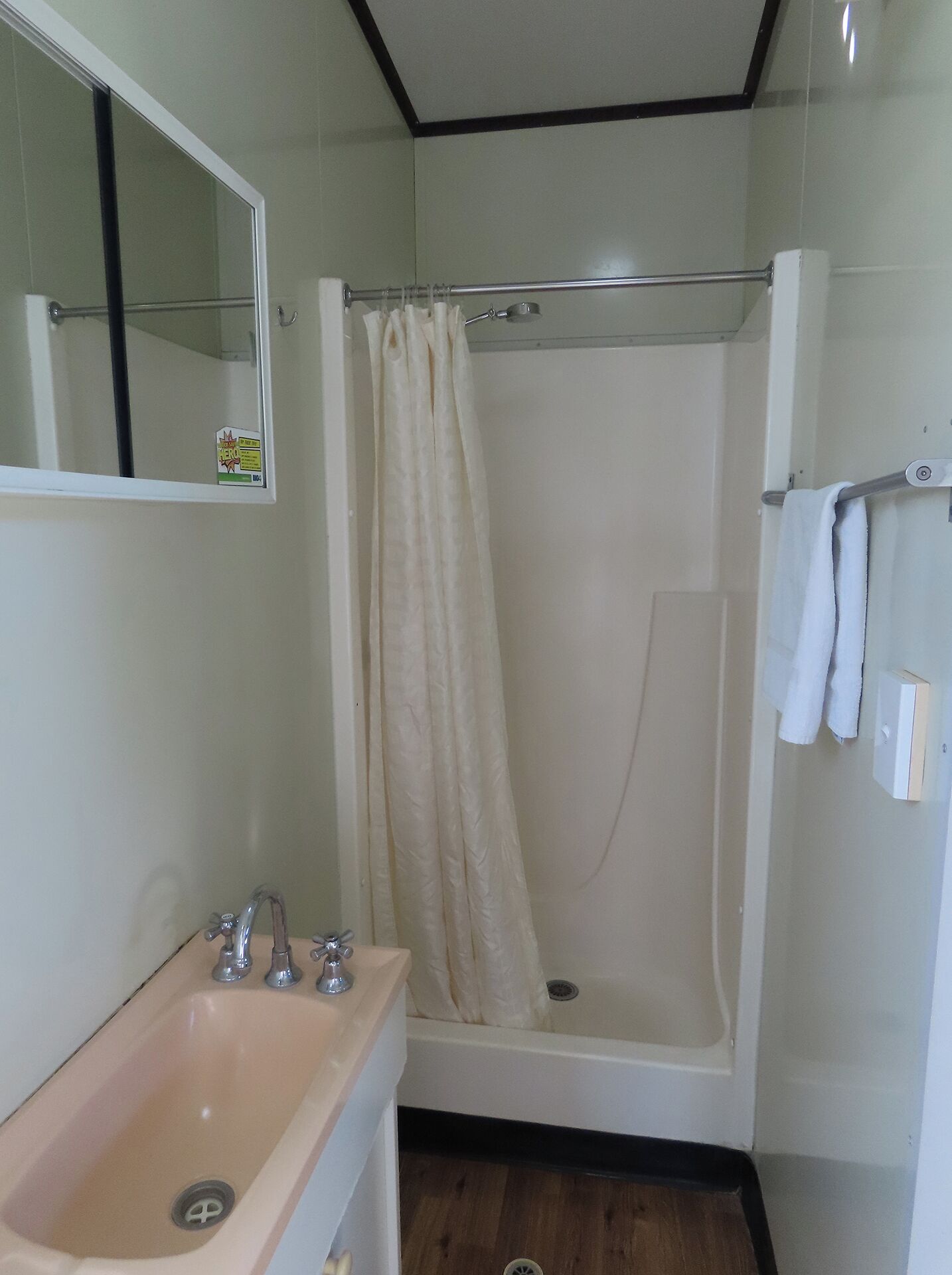 Un baño con lavamanos, espejo, ducha y perchero para toallas.