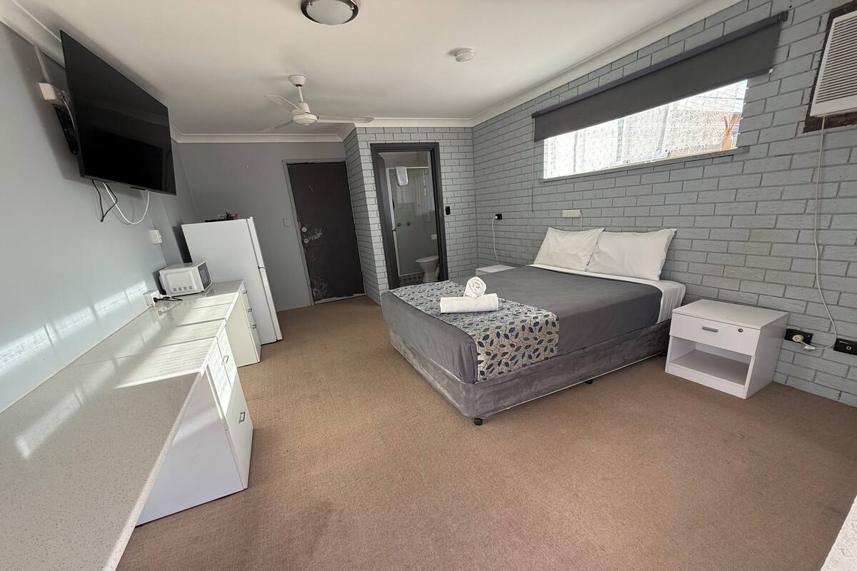 Une chambre à coucher avec un lit, des tables de chevet, une télévision, un bureau et une fenêtre.