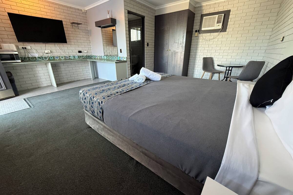 Une chambre d’hôtel équipée d’un lit, d’un bureau, d’une chaise, d’un téléviseur à écran plat et d’une kitchenette.