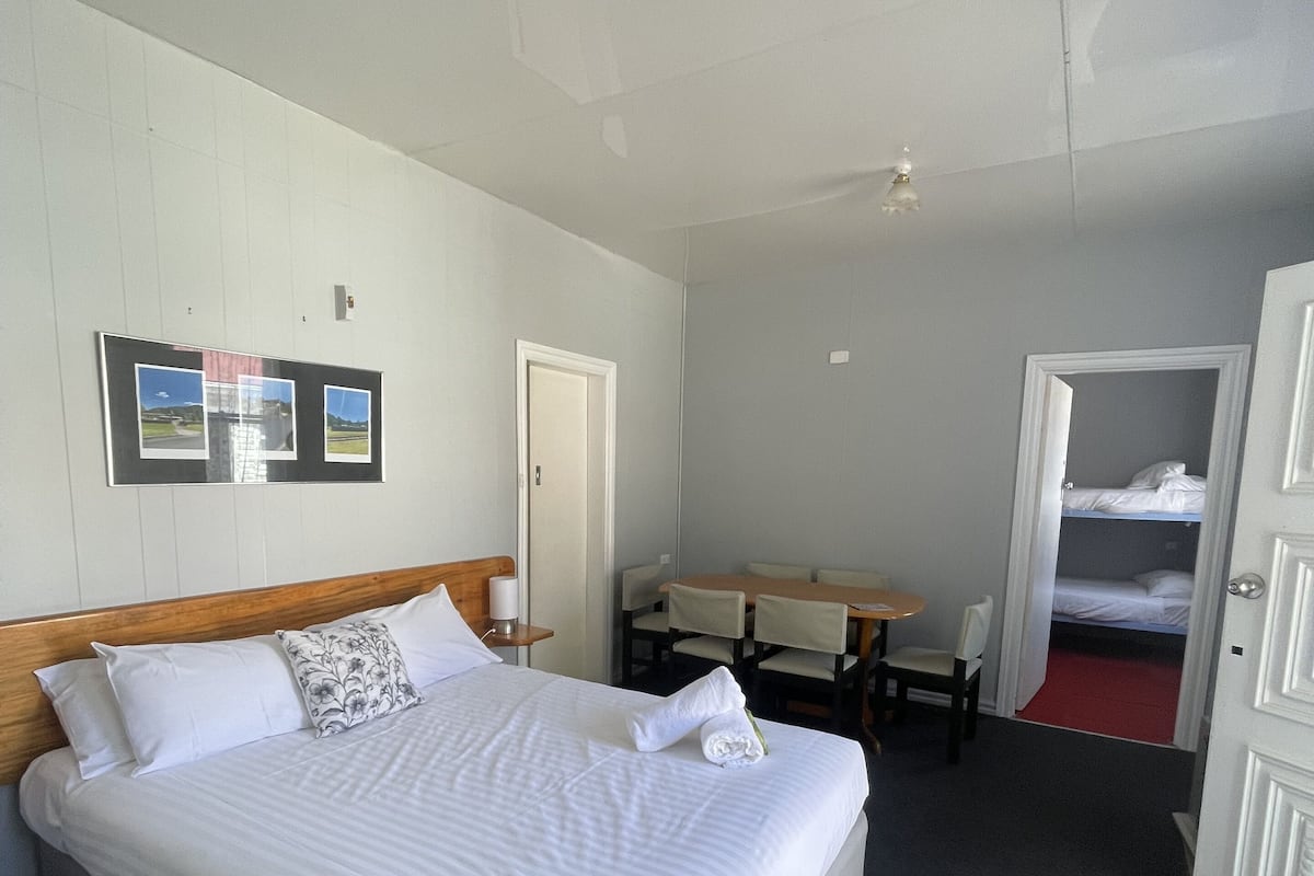 A hotel room with a large bed, a desk, and a chair. There is a door leading to a balcony.