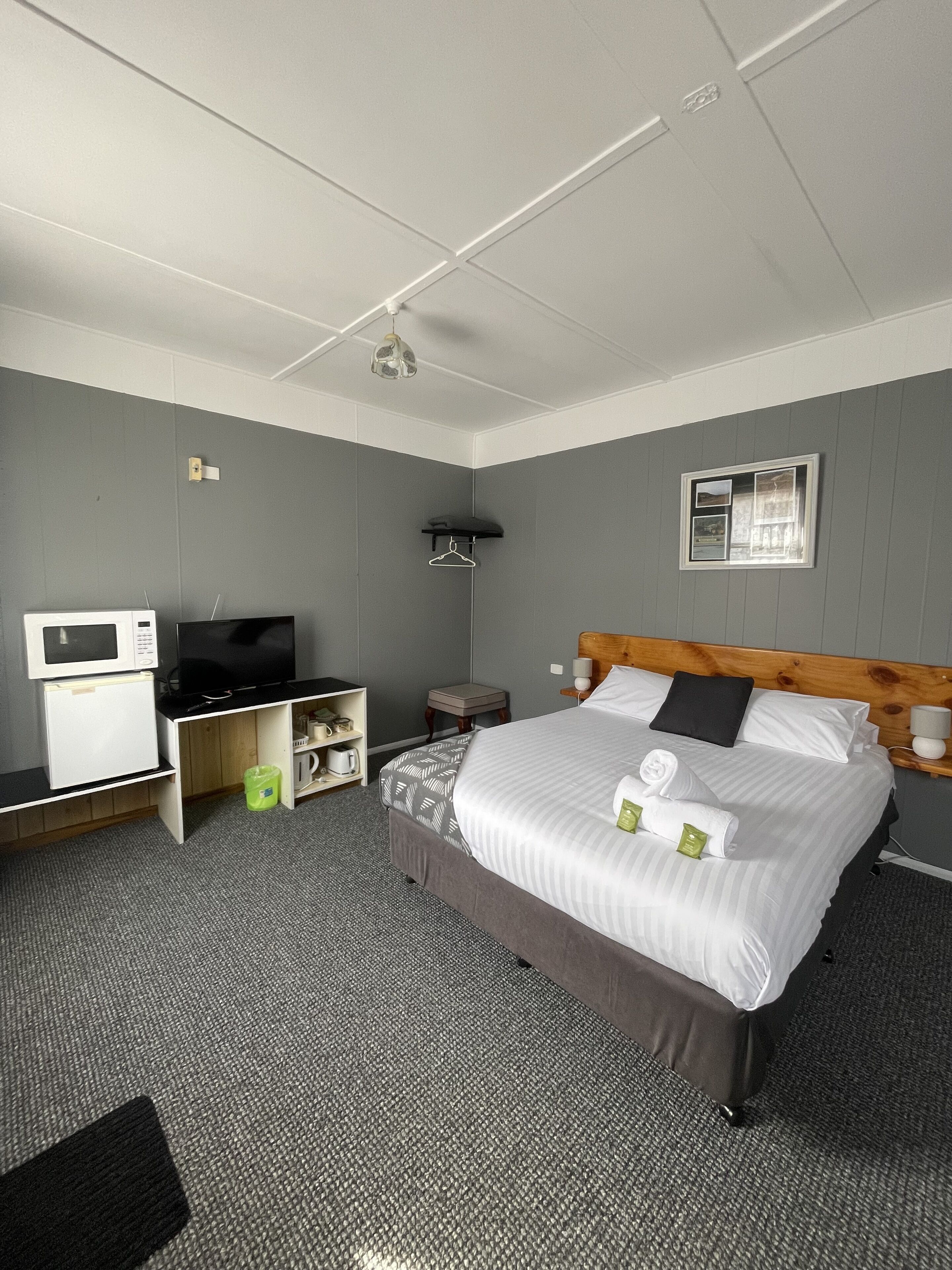 Una camera d'albergo con un letto, una televisione, un forno a microonde, un tavolino e una mensola.