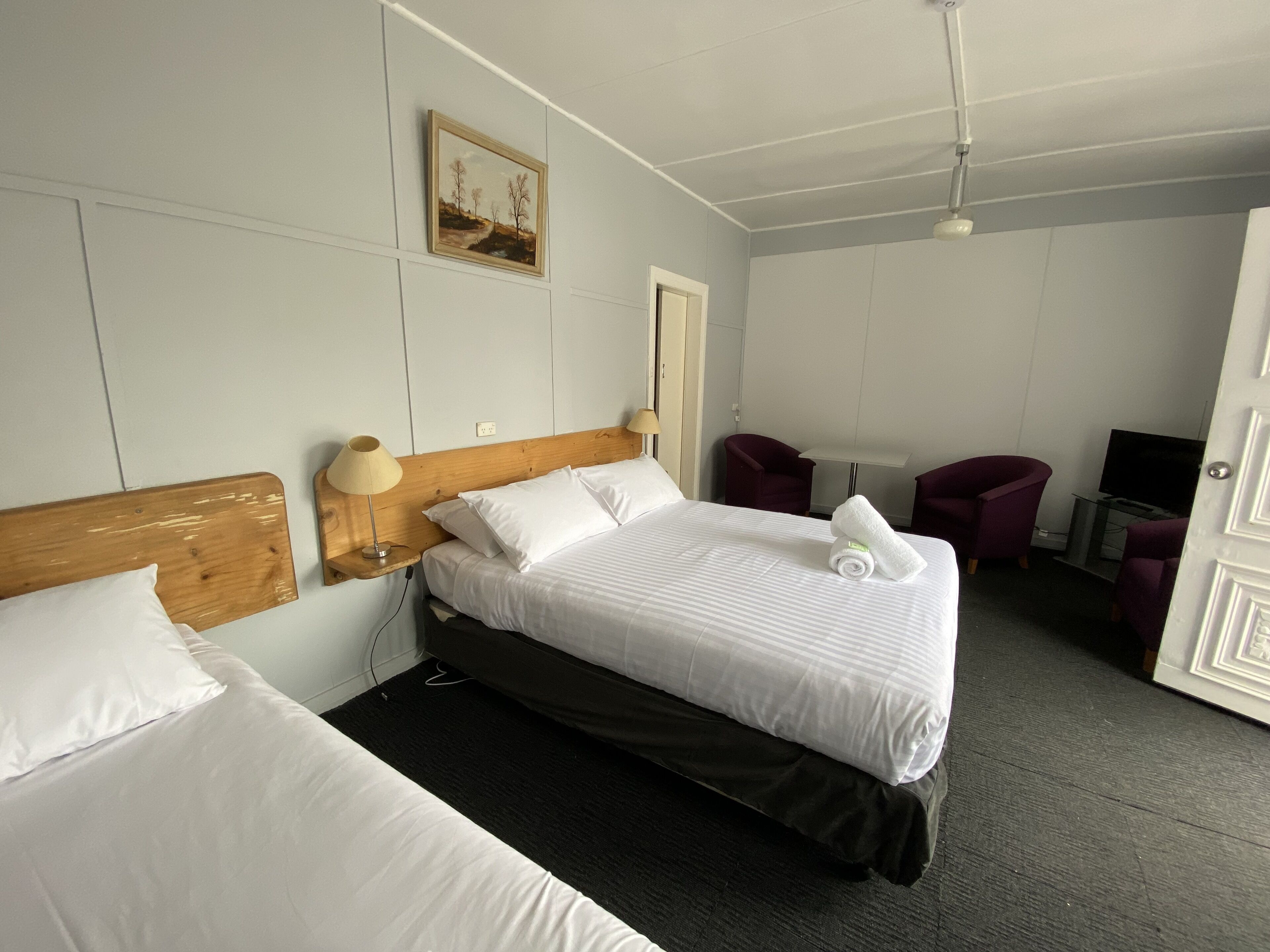 A hotel room with two beds, a painting on the wall, a desk with a chair, and a TV.