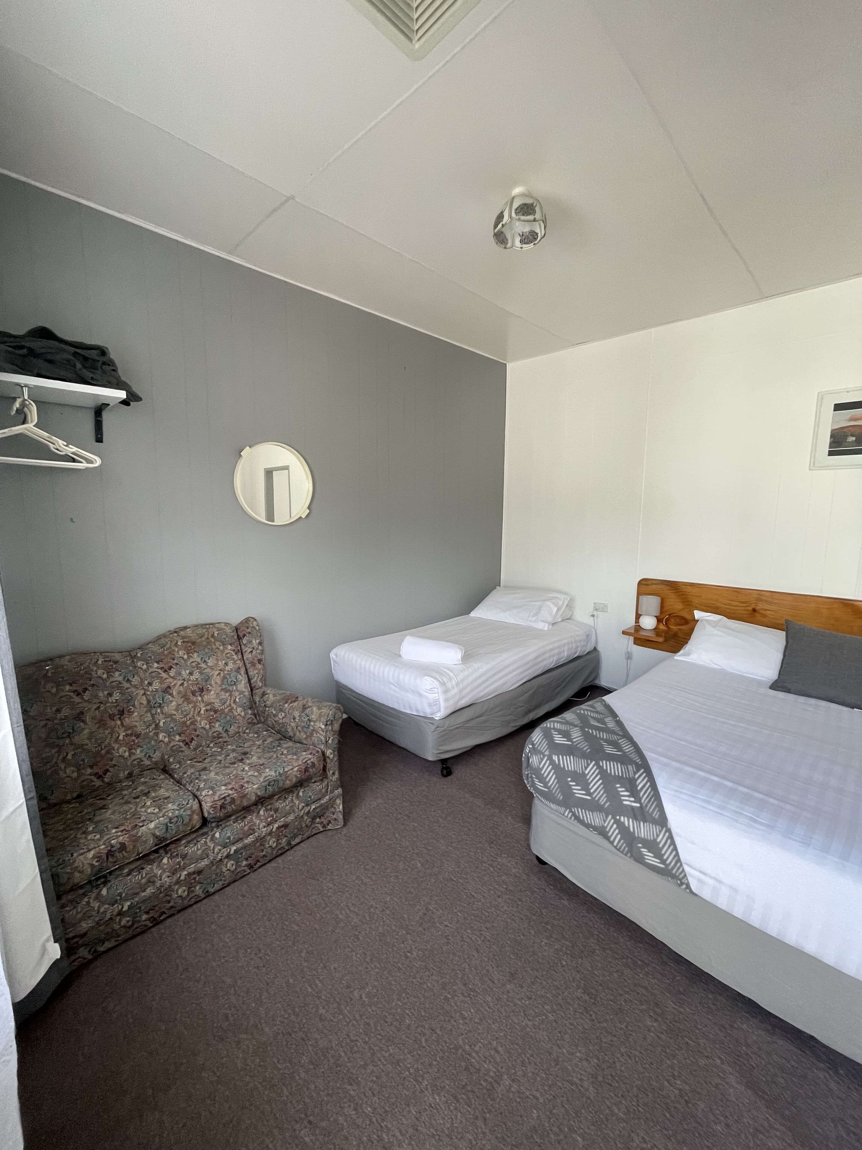 Habitación de hotel con una cama individual, un sofá, una mesita y un espejo fijado a la pared.
