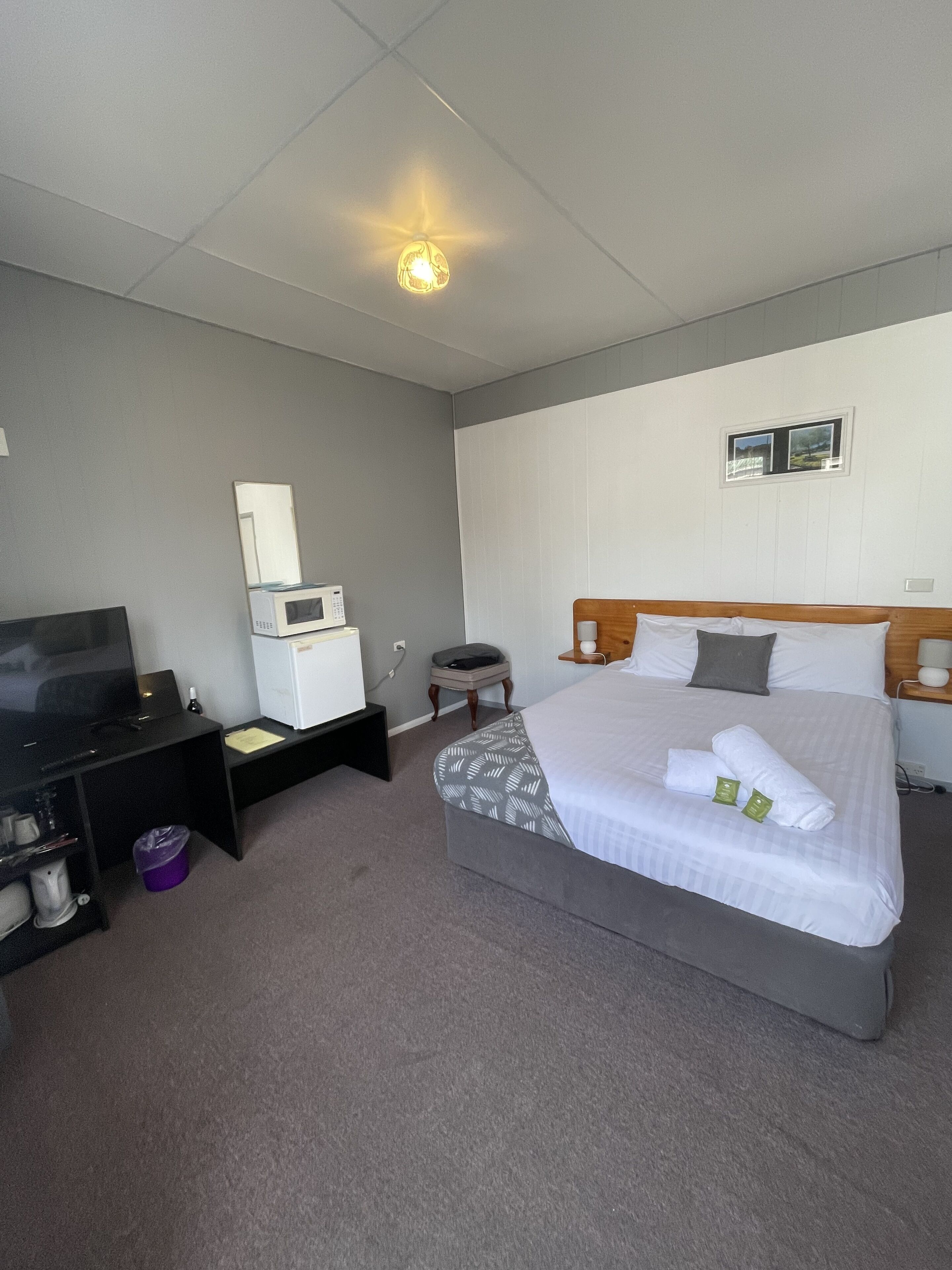 A hotel room with a bed, a TV, a microwave, a small table, and a window.