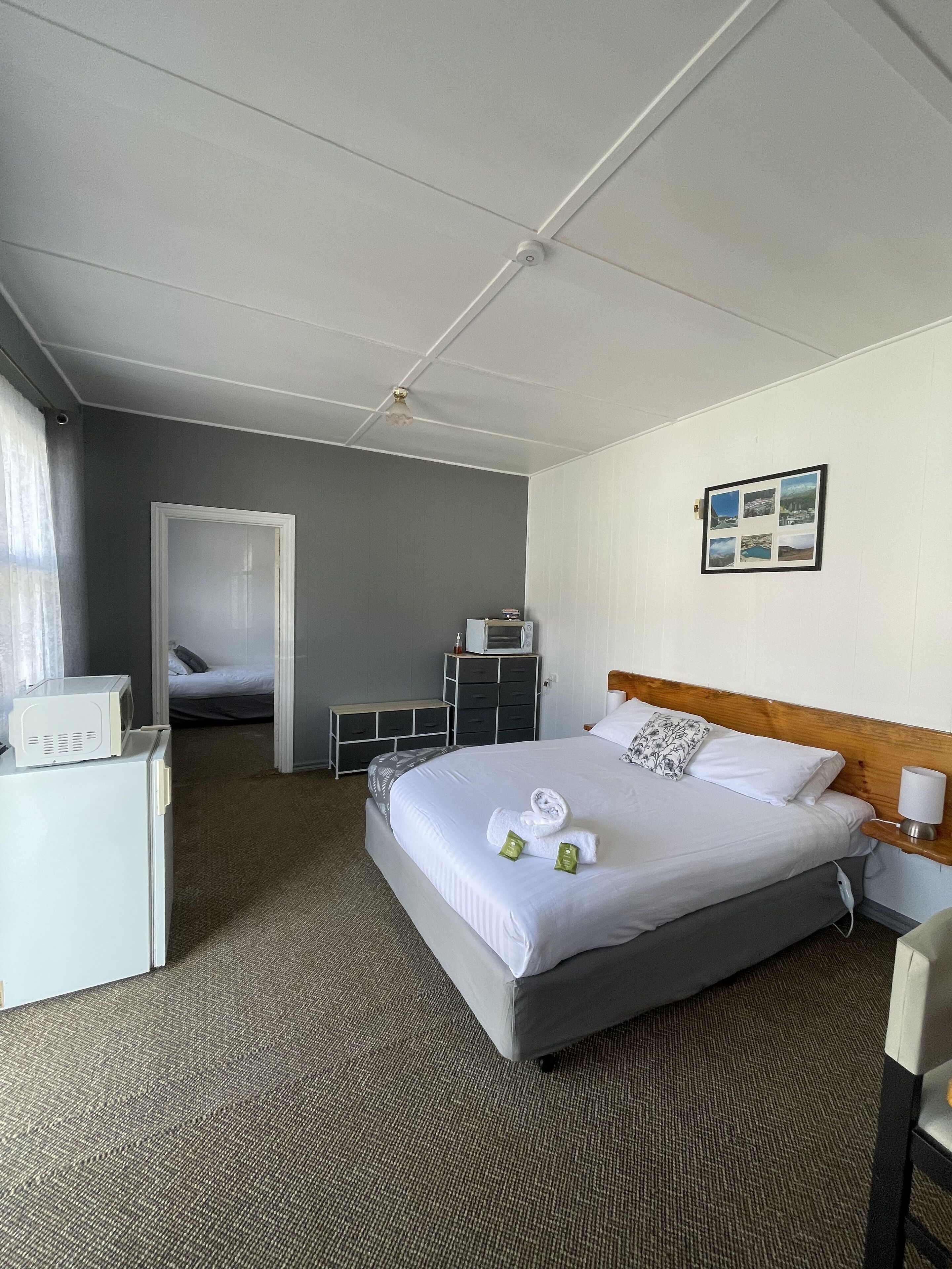 A hotel room with a large bed, a bedside table with a lamp, a microwave, a small desk, and a wardrobe.
