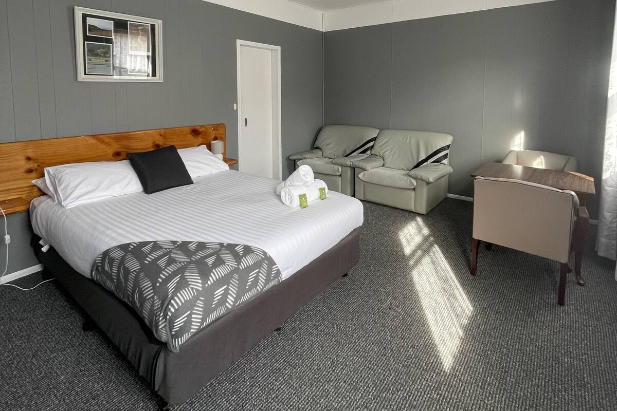 A hotel room with a large bed, a desk, a chair, and a sofa.