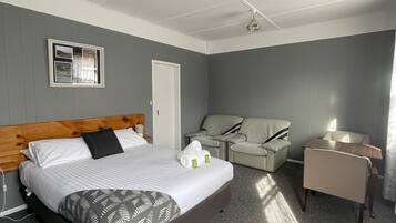 A hotel room with a large bed, a desk, a chair, and a sofa.