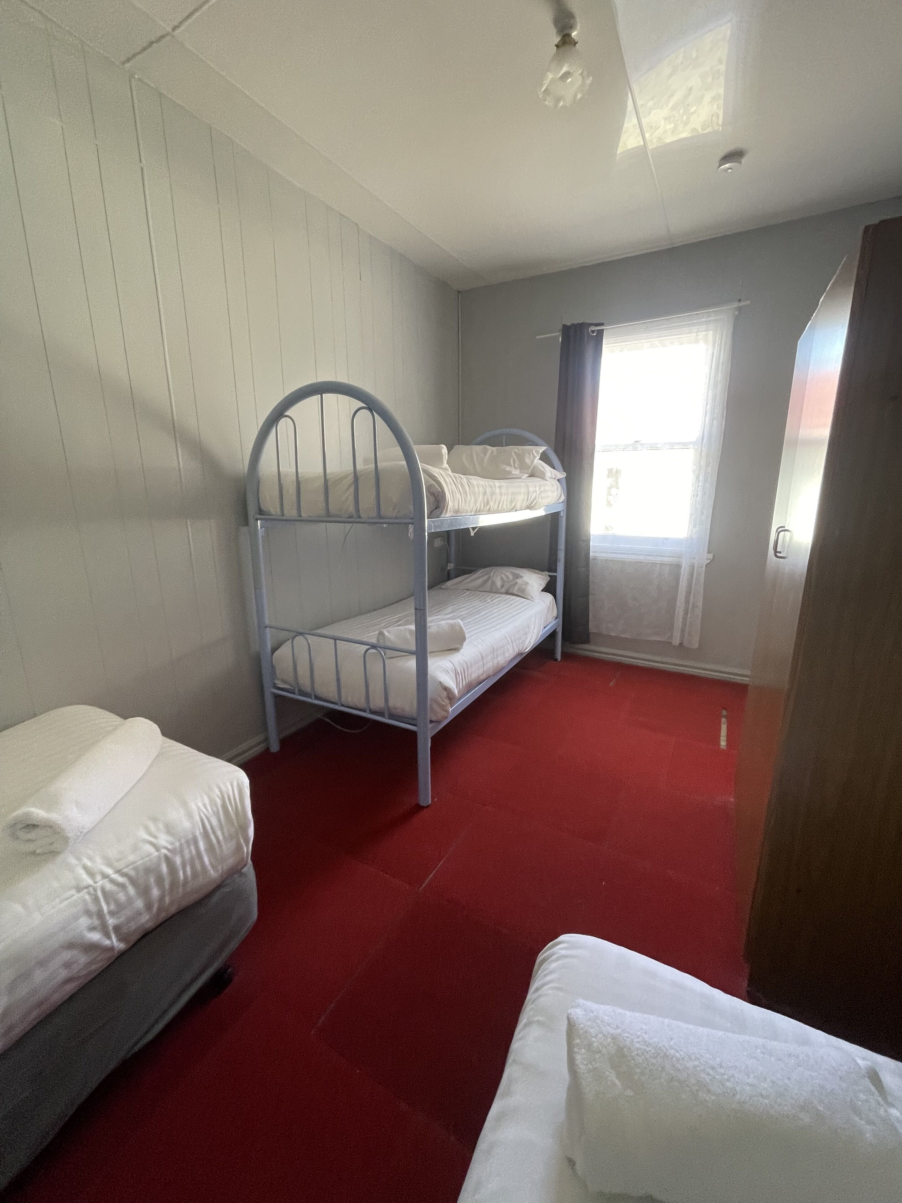 Ein Schlafsaalzimmer mit Etagenbetten, einem Vorhangfenster und einem roten Teppichboden.
