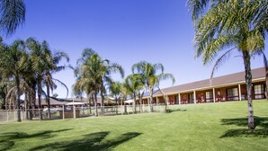 A hotel with a red roof, multiple rooms, and a fenced outdoor area with palm trees. - Tocumwal Golf Resort (Tocumwal)