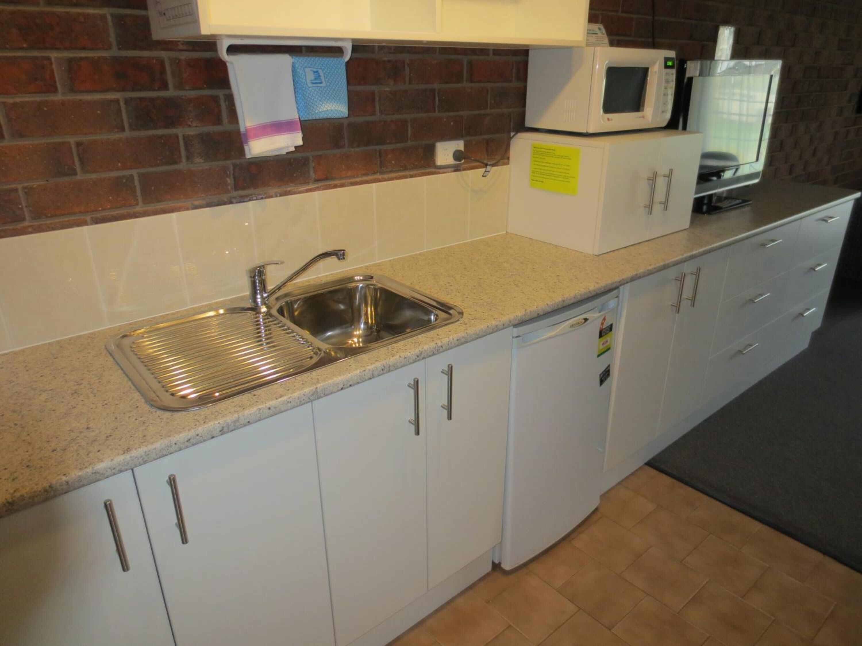 A kitchen with a stainless steel sink, white cabinets, a microwave, and a small refrigerator.