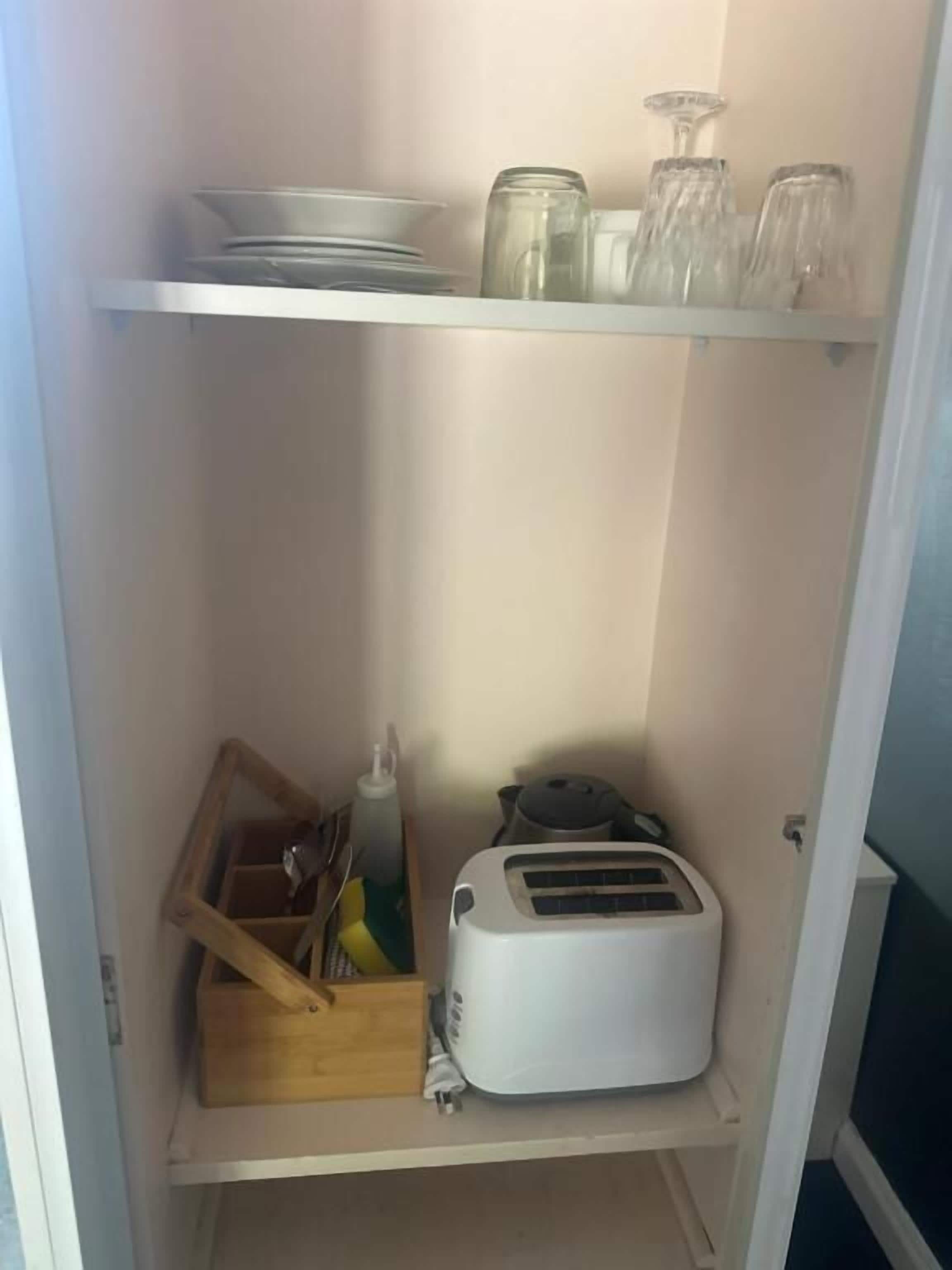 Una cocina con un tostador, una caja de madera y cristalería en los estantes.