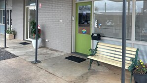 A building entrance with a green door, a bench, and a potted plant. - Memphis Motor Inn (Parkes)