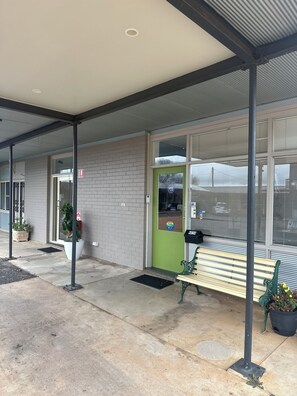 Entrada de un edificio con una puerta verde, un banco y una planta en maceta.
