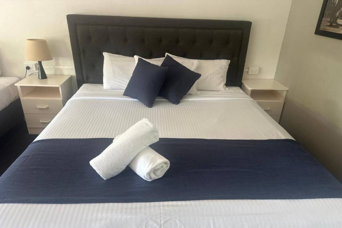 A neatly made bed with white and navy bedding, a folded towel, and a dark headboard.