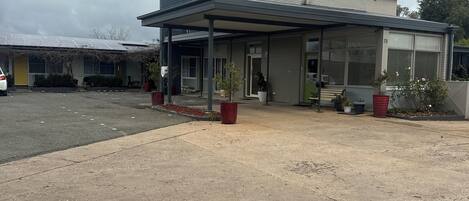 A building with a covered entrance, potted plants, and a parking lot.