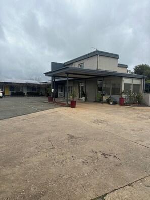 A building with a covered entrance, potted plants, and a parking lot.