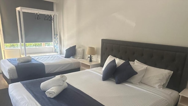 A hotel room with two beds, each with a white and blue bedspread, a dark headboard, and a nightstand with a lamp.