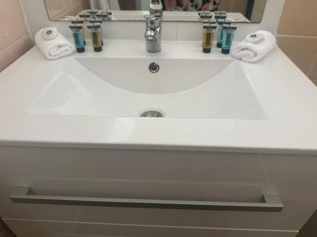 A white bathroom sink with a mirror above it, two towels, and several toiletries on the counter.