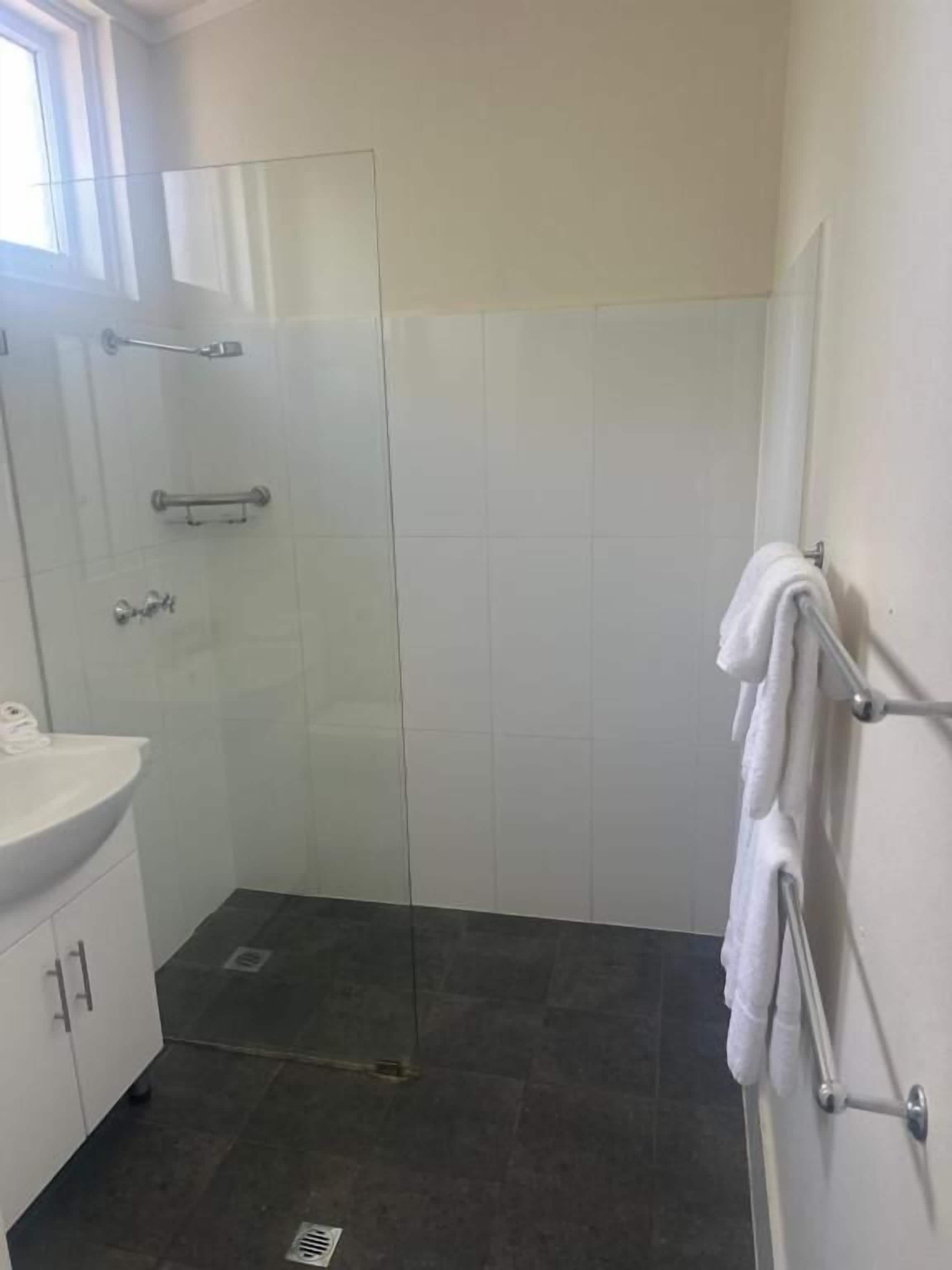 A small, modern bathroom with a glass shower enclosure, a white sink, and a towel rack.