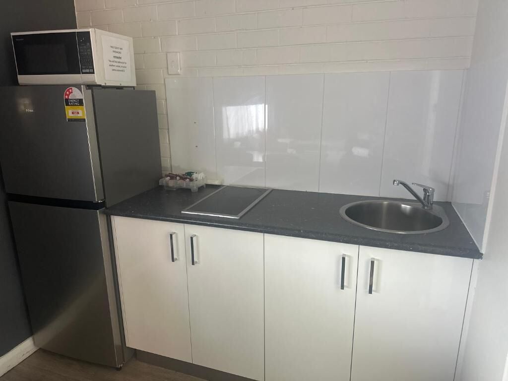 Una cocina con un refrigerador de acero inoxidable, un microondas, un lavamanos y armarios blancos.