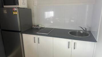 Una cocina con un refrigerador de acero inoxidable, un microondas, un lavamanos y armarios blancos.