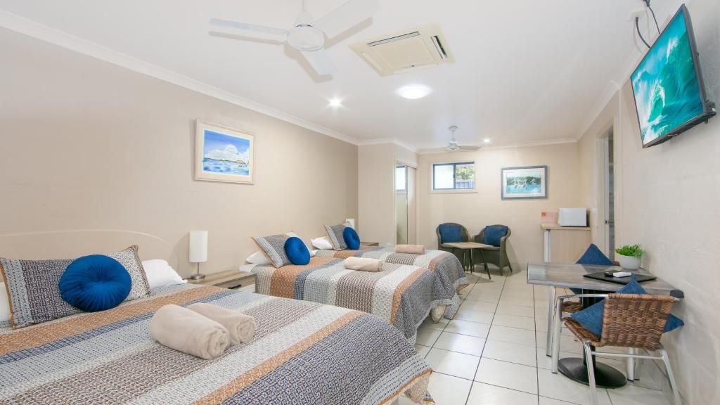 A hotel room with two beds, a desk, a chair, a television, and a ceiling fan.