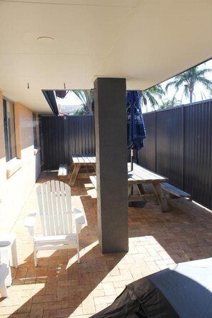 An outdoor patio area with a covered seating area, a table, and a white Adirondack chair. - Yamba Twin Pines Motel (Yamba)