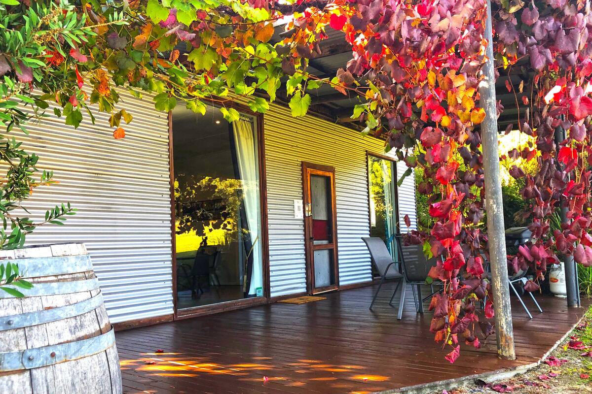 A wooden deck with a covered porch, a rustic barrel, and a building with a sliding glass door.