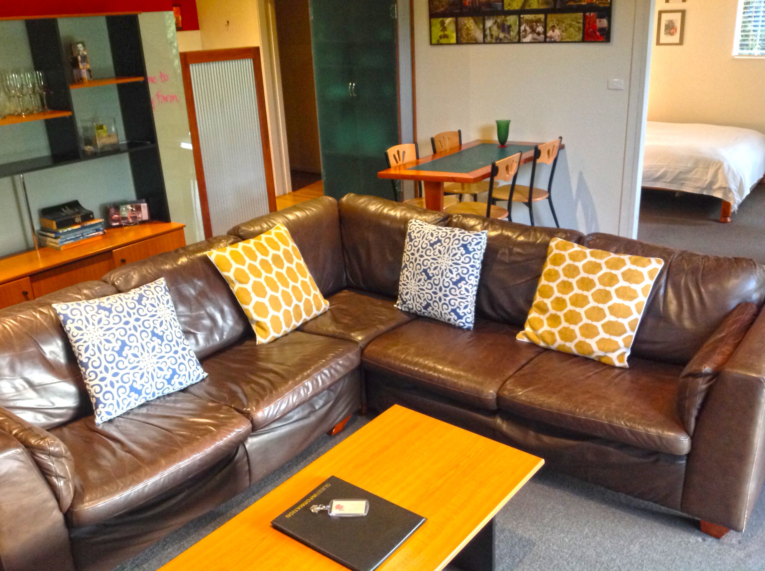 A brown leather sofa with patterned cushions, a wooden coffee table, and a dining table with chairs in the background.